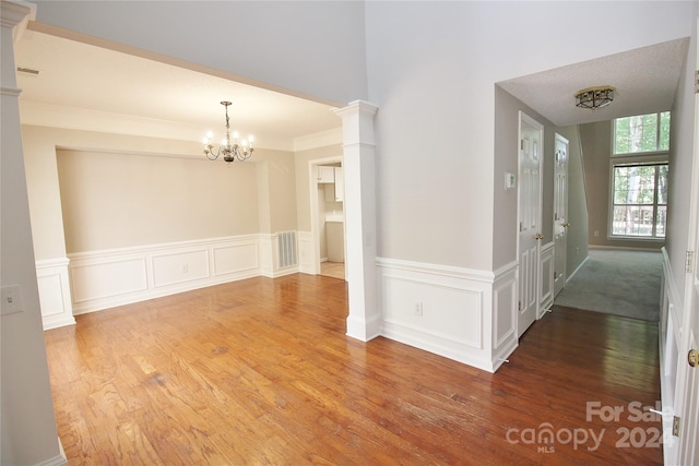 empty room featuring hardwood / wood-style flooring, an inviting chandelier, and decorative columns