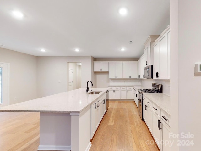 kitchen featuring a center island with sink, sink, light wood-type flooring, white cabinetry, and appliances with stainless steel finishes