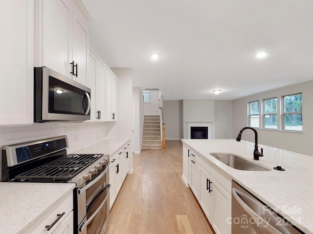 kitchen with appliances with stainless steel finishes, white cabinetry, light stone countertops, light hardwood / wood-style flooring, and sink