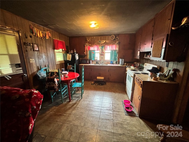 kitchen with black refrigerator, wood walls, sink, and white electric stove