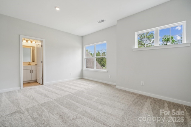 unfurnished bedroom featuring multiple windows, ensuite bathroom, and light carpet