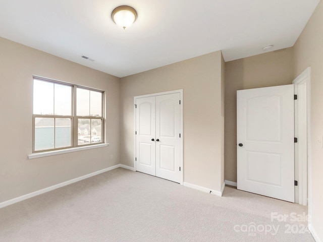 unfurnished bedroom with light colored carpet and a closet