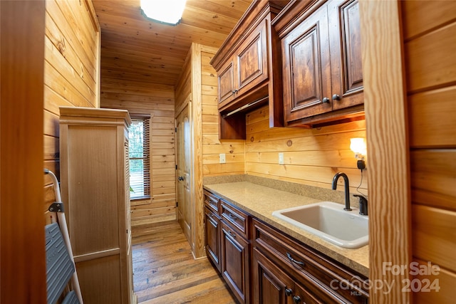 kitchen featuring light stone counters, wood ceiling, sink, wooden walls, and light hardwood / wood-style floors