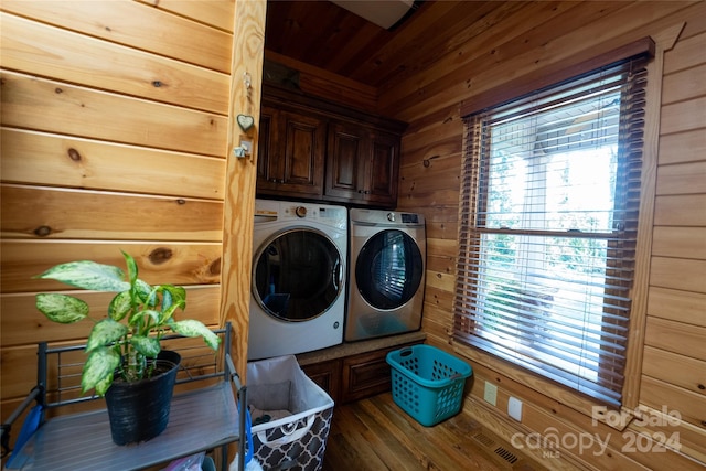 clothes washing area featuring separate washer and dryer, wooden walls, dark hardwood / wood-style floors, and cabinets