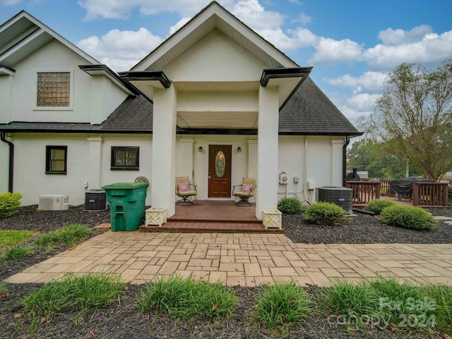 view of front of home with a shingled roof, stucco siding, covered porch, and central AC unit