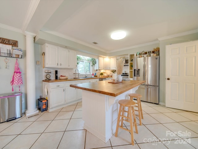 kitchen with a kitchen breakfast bar, butcher block countertops, stainless steel appliances, ornate columns, and ornamental molding