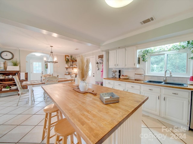 kitchen with a sink, light tile patterned floors, white cabinets, and ornamental molding