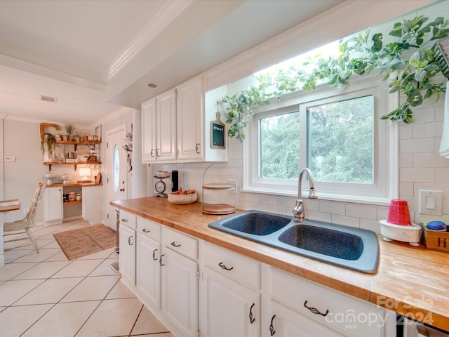 kitchen with decorative backsplash, white cabinets, wooden counters, ornamental molding, and sink