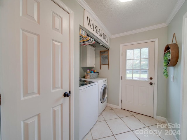 laundry area with ornamental molding, a textured ceiling, washing machine and clothes dryer, cabinet space, and light tile patterned floors
