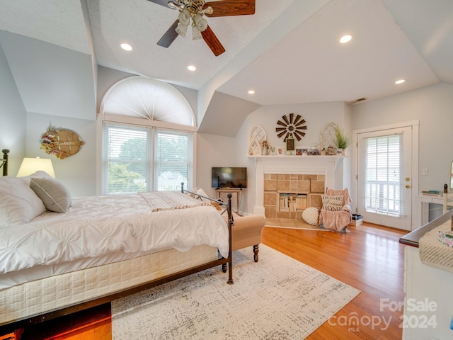 bedroom featuring access to outside, ceiling fan, wood-type flooring, a fireplace, and vaulted ceiling