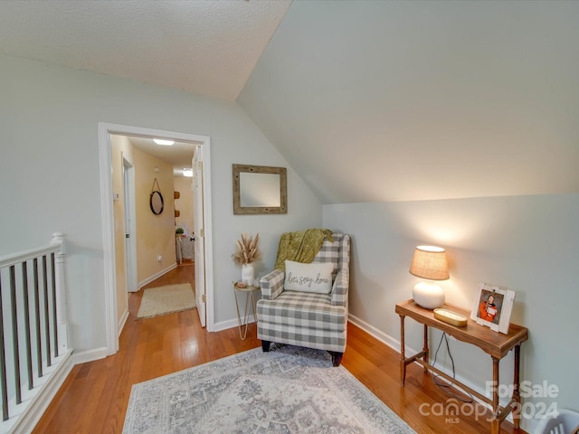 living area featuring a textured ceiling, light hardwood / wood-style floors, and lofted ceiling