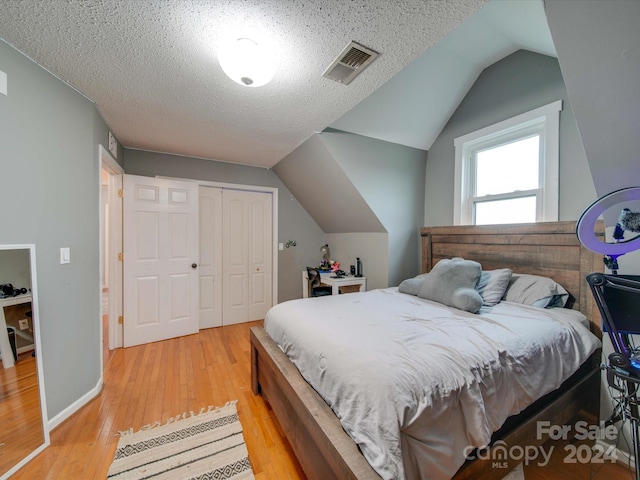 bedroom with a textured ceiling, light wood-type flooring, a closet, and lofted ceiling