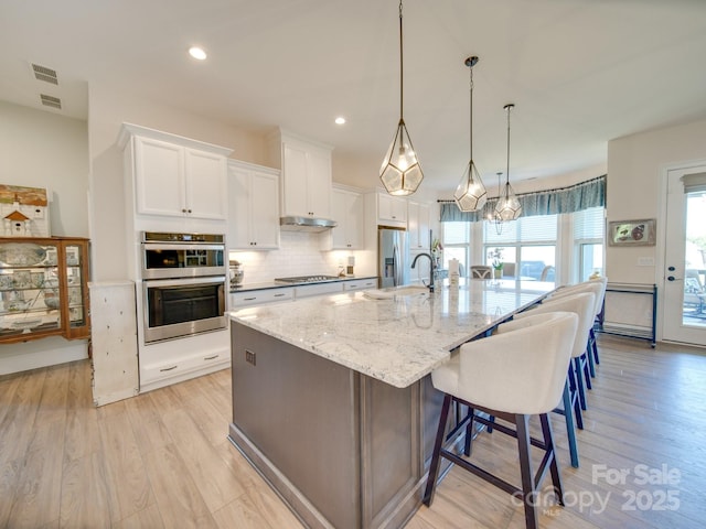 kitchen with light stone countertops, a spacious island, white cabinetry, pendant lighting, and stainless steel appliances