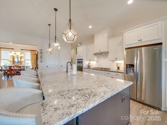 kitchen with light stone countertops, appliances with stainless steel finishes, a large island, white cabinets, and pendant lighting