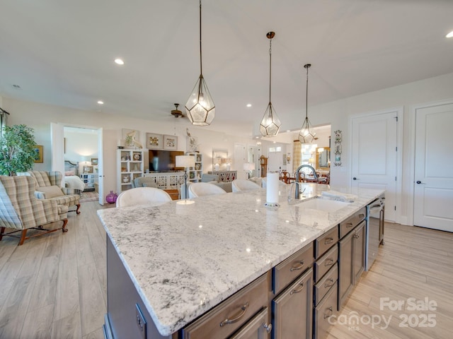 kitchen with stainless steel dishwasher, sink, pendant lighting, light stone counters, and a center island with sink