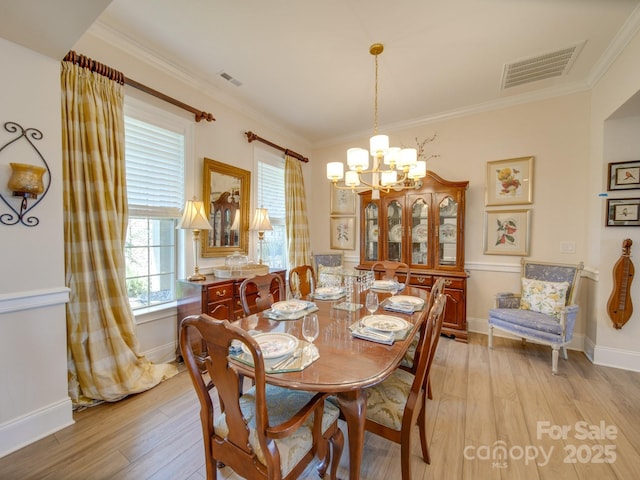 dining area with light hardwood / wood-style flooring, crown molding, and an inviting chandelier