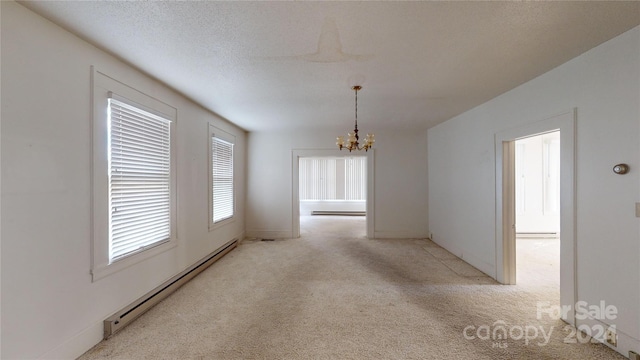 carpeted empty room featuring a textured ceiling, baseboard heating, and a chandelier