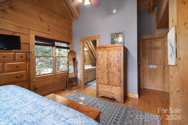 bedroom featuring wood walls, connected bathroom, lofted ceiling with beams, ceiling fan, and light wood-type flooring