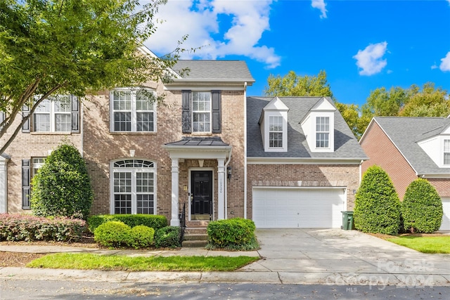 colonial home with roof with shingles, concrete driveway, an attached garage, and brick siding