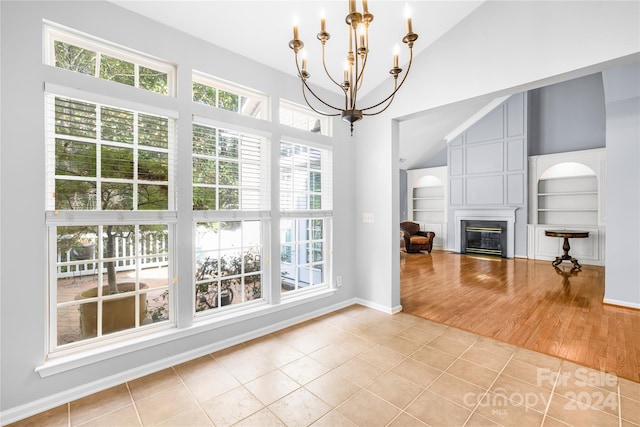 unfurnished living room with a glass covered fireplace, a healthy amount of sunlight, built in features, and a notable chandelier