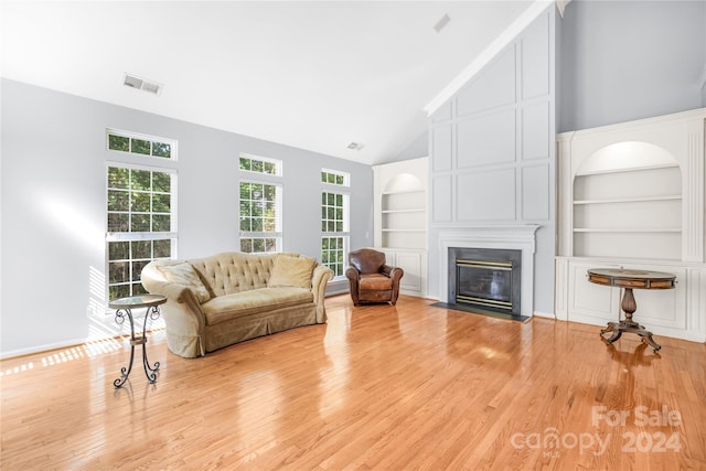 living area with a fireplace with flush hearth, visible vents, vaulted ceiling, wood finished floors, and built in shelves