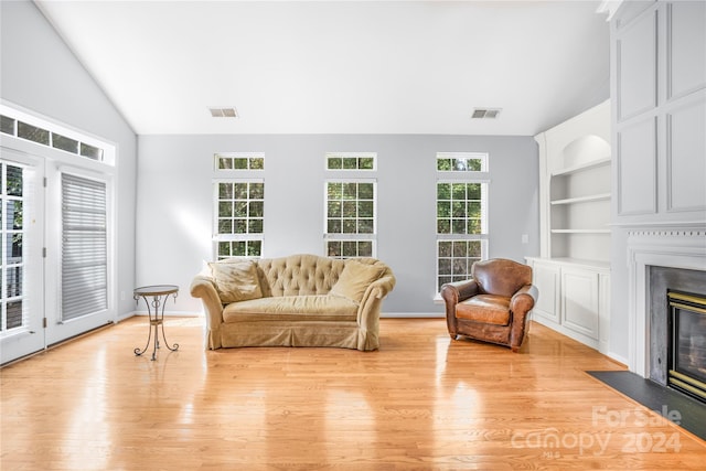 interior space with lofted ceiling, a fireplace with flush hearth, light wood-style flooring, visible vents, and built in features