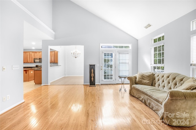 living room with a notable chandelier, light wood-type flooring, plenty of natural light, and high vaulted ceiling