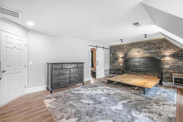 bedroom featuring wooden walls, light wood-type flooring, crown molding, and a barn door