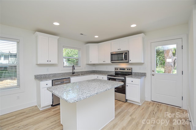 kitchen featuring white cabinets, a kitchen island, stainless steel appliances, light stone countertops, and light hardwood / wood-style floors