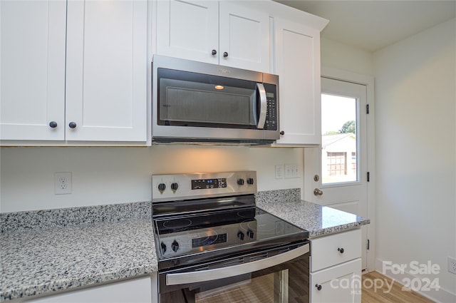 kitchen with wood-type flooring, light stone countertops, stainless steel appliances, and white cabinetry