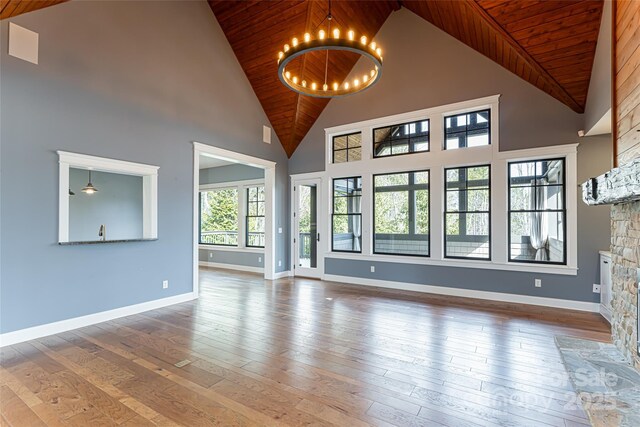 unfurnished living room with a stone fireplace, hardwood / wood-style floors, wood ceiling, and a chandelier