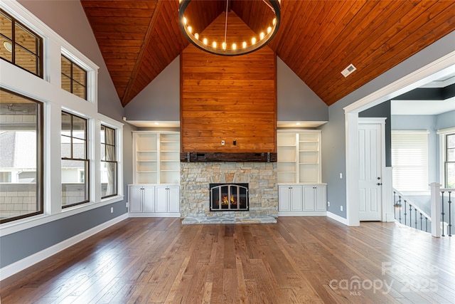 unfurnished living room with wood-type flooring, plenty of natural light, wooden ceiling, and a stone fireplace