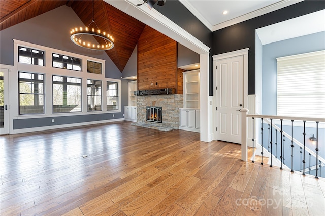 unfurnished living room with hardwood / wood-style flooring, a stone fireplace, a chandelier, and high vaulted ceiling