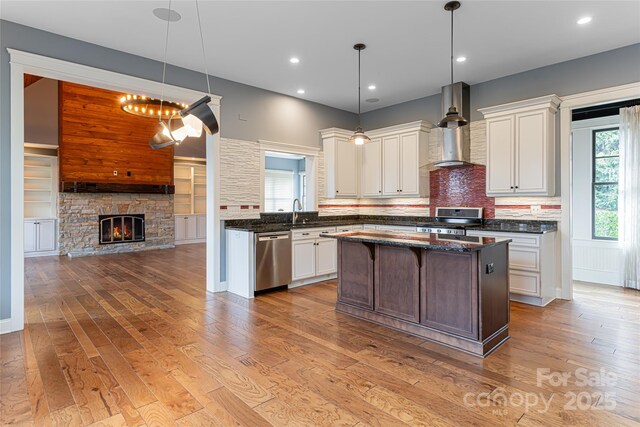 kitchen featuring stainless steel appliances, hanging light fixtures, a center island, and wall chimney range hood