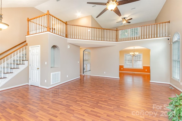 unfurnished living room featuring hardwood / wood-style flooring, ceiling fan with notable chandelier, high vaulted ceiling, and a healthy amount of sunlight