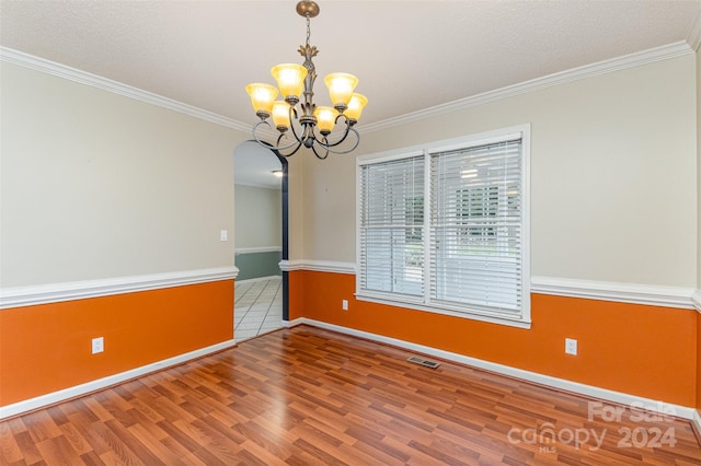 empty room featuring wood-type flooring, an inviting chandelier, crown molding, and a textured ceiling