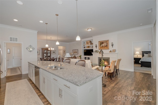 kitchen featuring white cabinets, an island with sink, sink, hanging light fixtures, and light stone counters