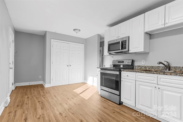 kitchen featuring stainless steel appliances, sink, white cabinetry, dark stone countertops, and light wood-type flooring