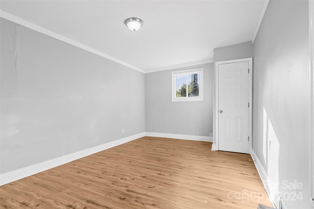 spare room with light wood finished floors, crown molding, and baseboards