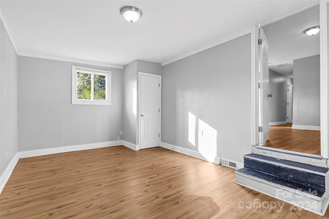 spare room with crown molding, wood finished floors, visible vents, and baseboards