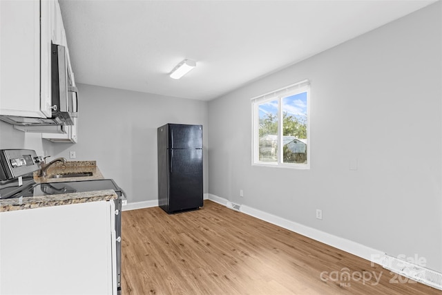 kitchen featuring light wood-type flooring, white cabinetry, sink, black fridge, and stove