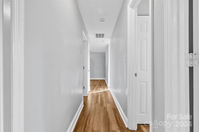 hallway with wood finished floors, visible vents, and baseboards