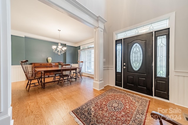 foyer entrance with hardwood / wood-style floors, decorative columns, ornamental molding, and a notable chandelier