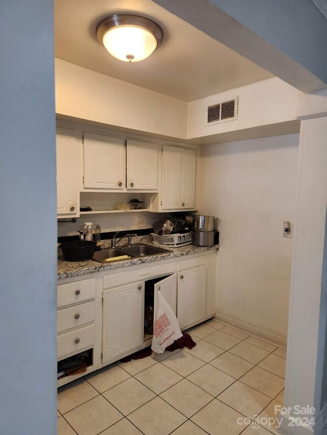 kitchen featuring white cabinets, light stone countertops, light tile patterned flooring, and sink