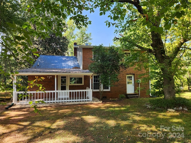 view of front facade with a porch, a chimney, entry steps, brick siding, and metal roof