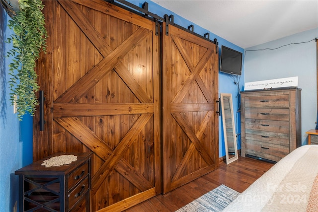 bedroom with a barn door and dark hardwood / wood-style flooring