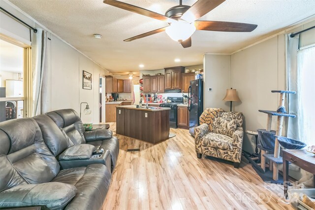 living room featuring light wood-type flooring, ceiling fan, a textured ceiling, and sink