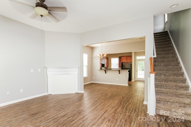 unfurnished living room with ceiling fan with notable chandelier and dark hardwood / wood-style flooring