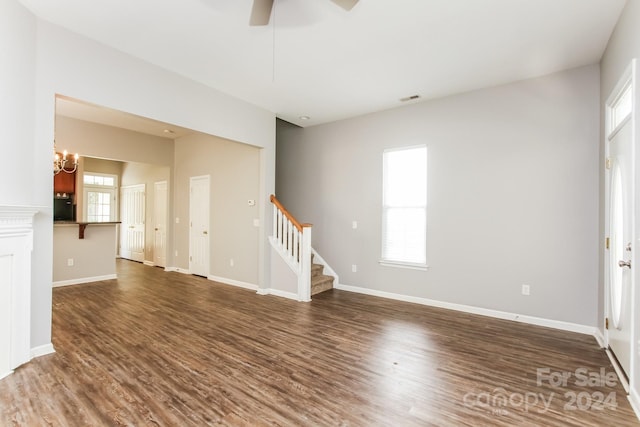 unfurnished room featuring ceiling fan with notable chandelier, plenty of natural light, and dark hardwood / wood-style floors