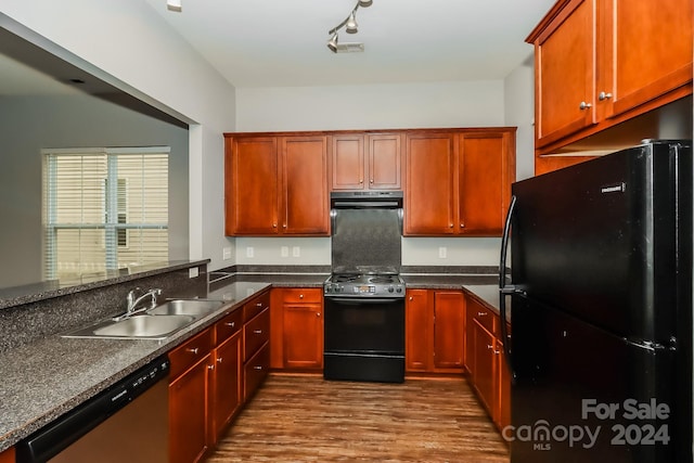 kitchen with black appliances, wood-type flooring, kitchen peninsula, sink, and dark stone counters